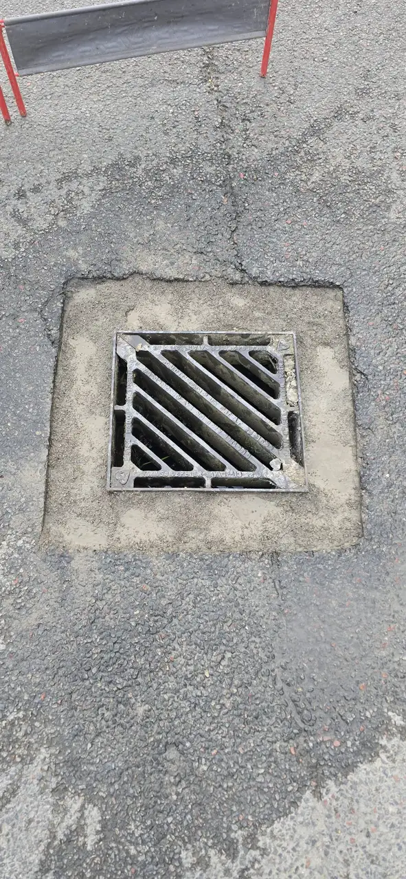 Reinstated cast-iron gully grate set in fresh tarmac
